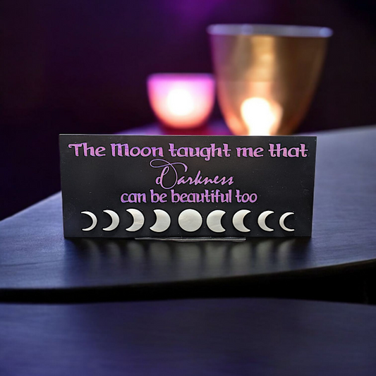 "Black tabletop sign with purple lettering reading 'The moon taught me that darkness can be beautiful too,' featuring a shimmering acrylic pearl moon phase — perfect for witches, moon lovers, or altar decor.