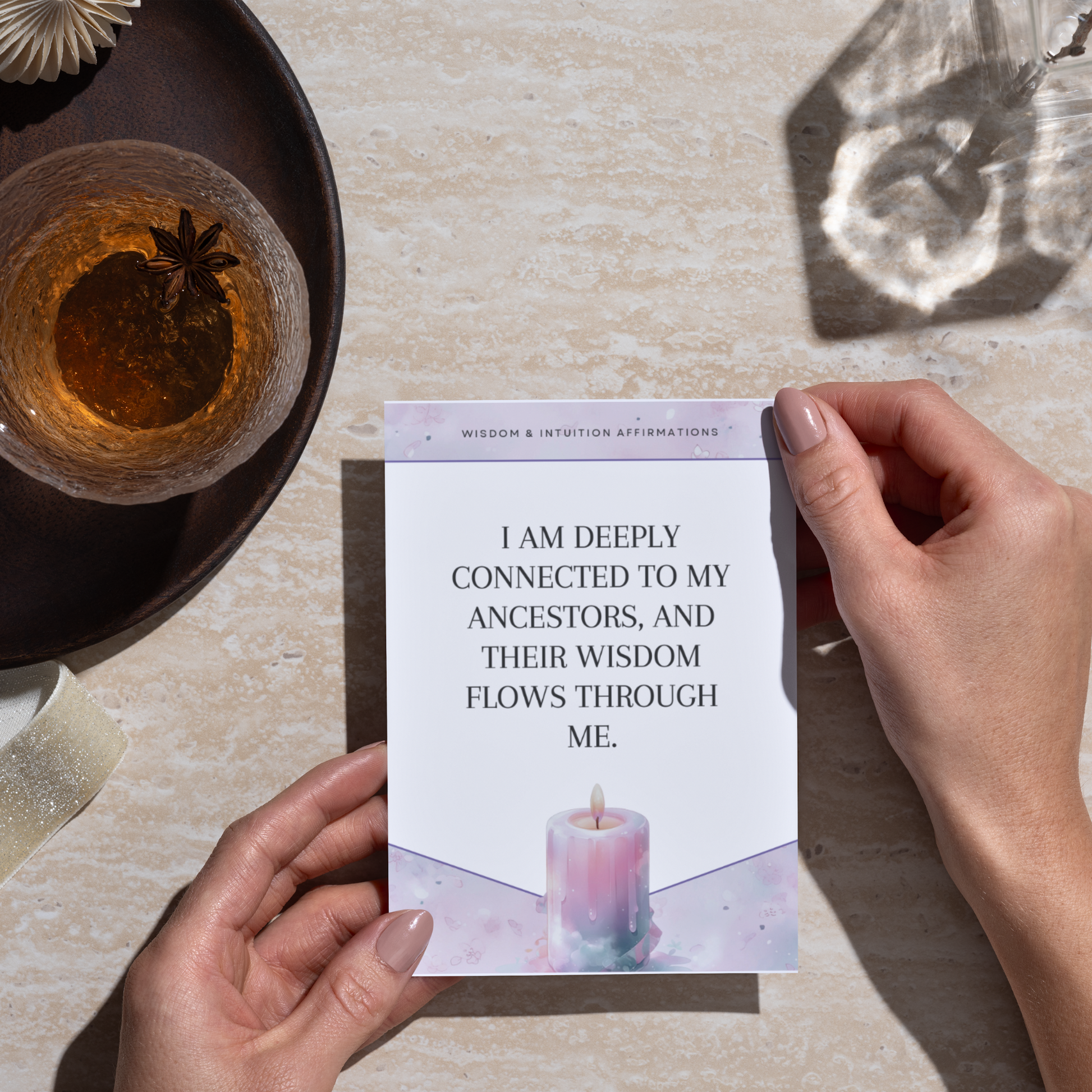 Person holding a printable affirmation card with an affirmation on a table with a candle and tea.